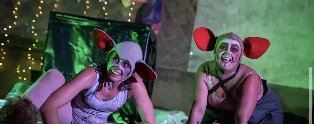 Two circus performers in playful mouse costumes under green stage lighting